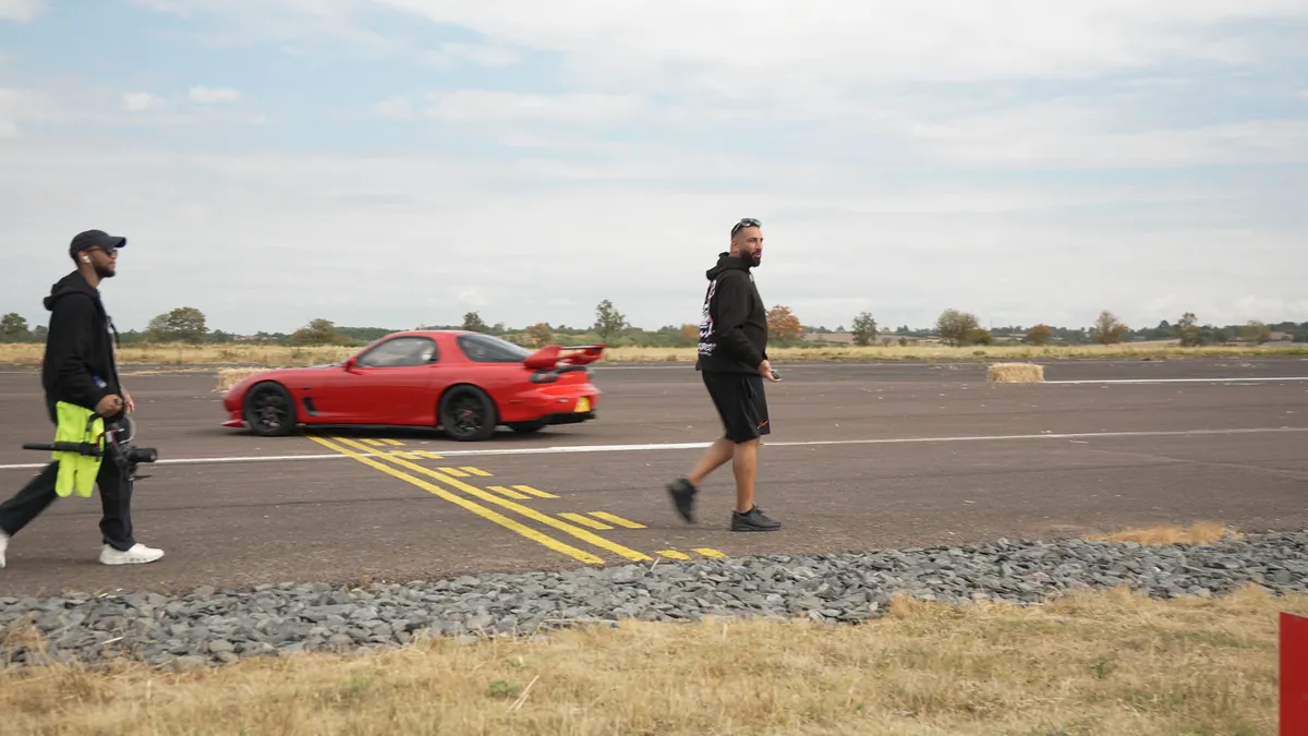 Two of us walking the verge with kit as a red car passes on the runway