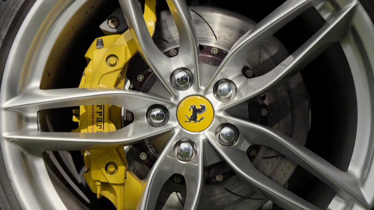 A yellow brake caliper behind a road car’s wheel in the paddock