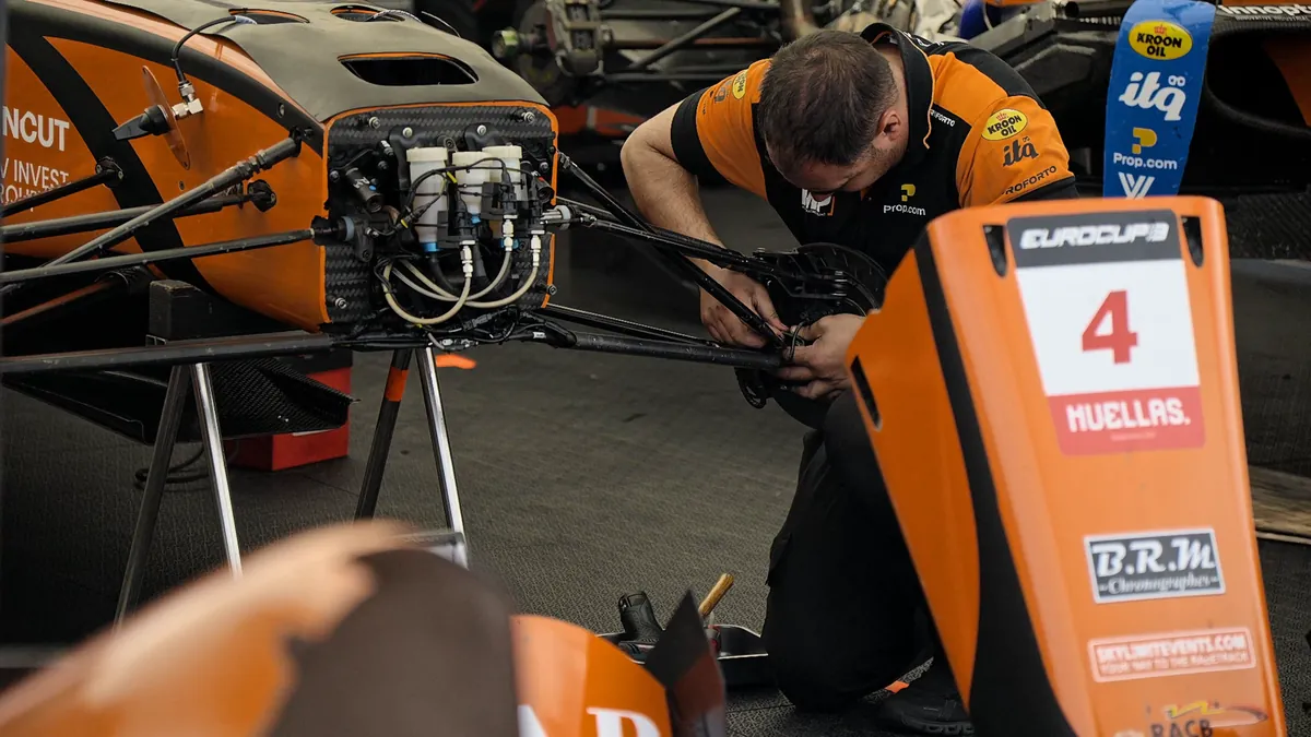 A mechanic in orange working on a car in the garage