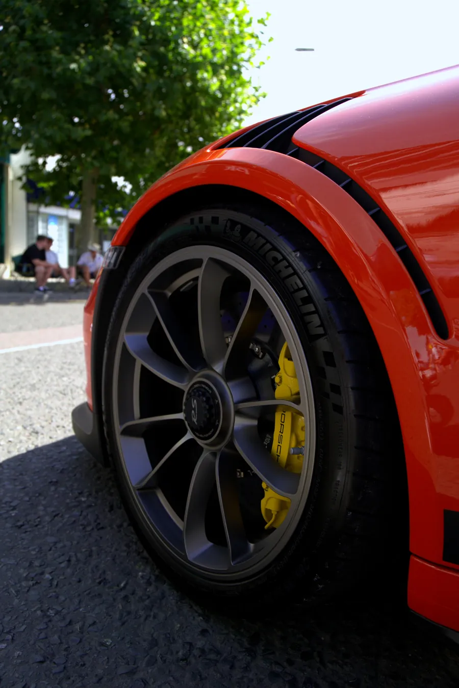 The wheel and yellow brake caliper of an orange Porsche
