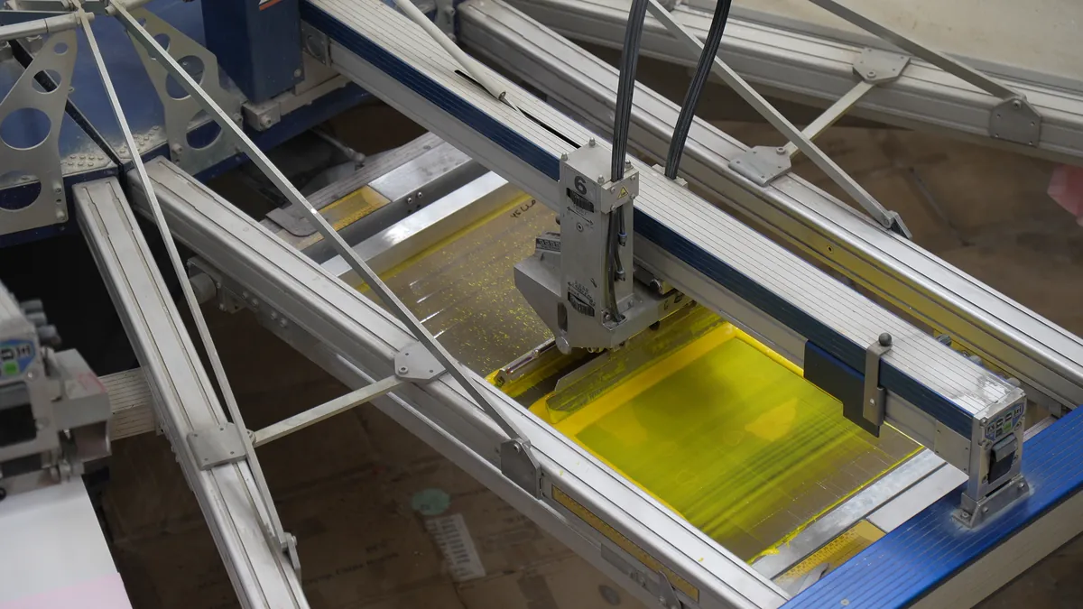 A squeegee pulling yellow ink across a screen
