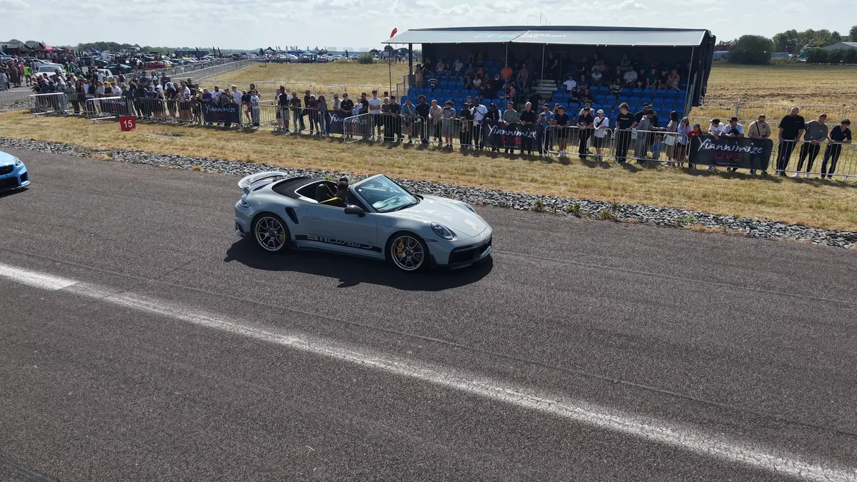 A silver convertible on the runway in front of the grandstand